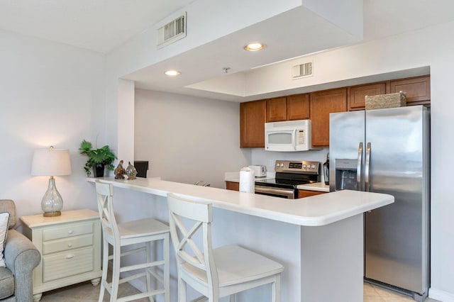 kitchen with a breakfast bar, light tile patterned floors, stainless steel appliances, and kitchen peninsula