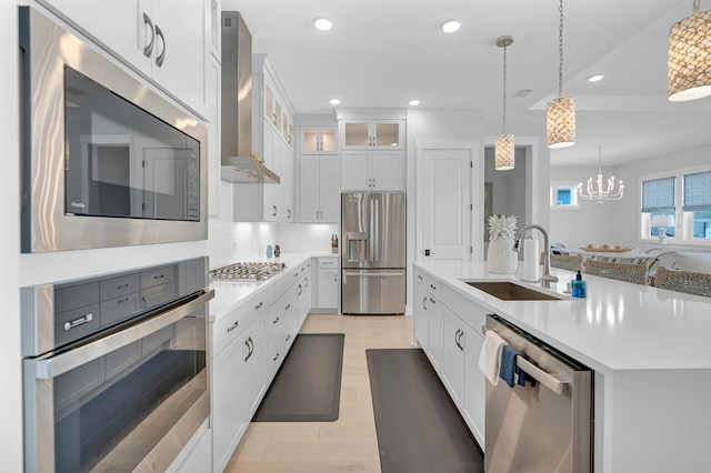 kitchen featuring white cabinets, stainless steel appliances, wall chimney range hood, and sink