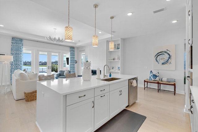 kitchen featuring light wood-type flooring, stainless steel dishwasher, sink, white cabinetry, and an island with sink