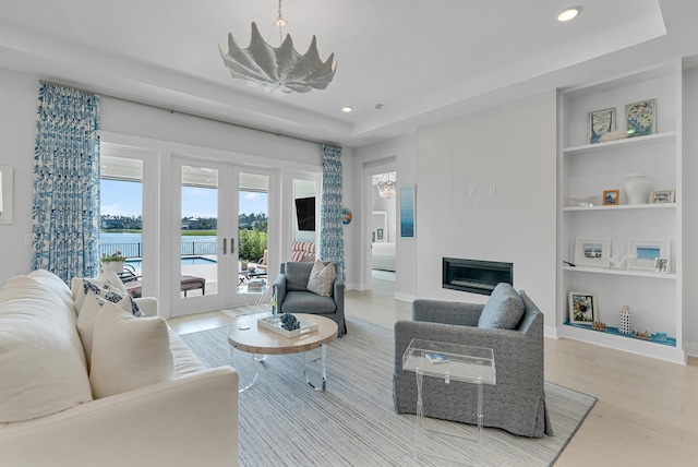 living room featuring a large fireplace, light hardwood / wood-style floors, french doors, and a notable chandelier