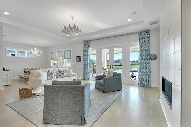 living room with a notable chandelier, light wood-type flooring, a tray ceiling, and french doors