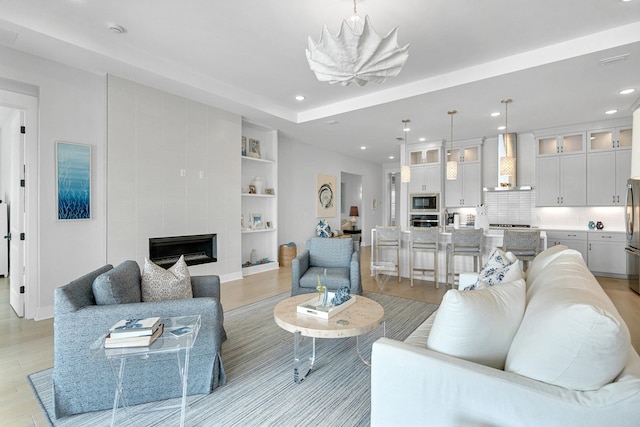 living room featuring a tiled fireplace, built in shelves, light hardwood / wood-style floors, and a notable chandelier