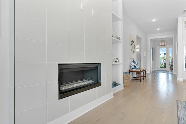 unfurnished living room with light hardwood / wood-style floors, a notable chandelier, and a tiled fireplace