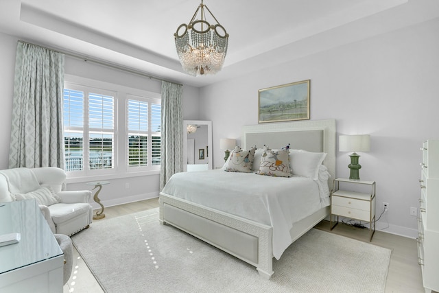 bedroom featuring a tray ceiling, a chandelier, and light hardwood / wood-style floors