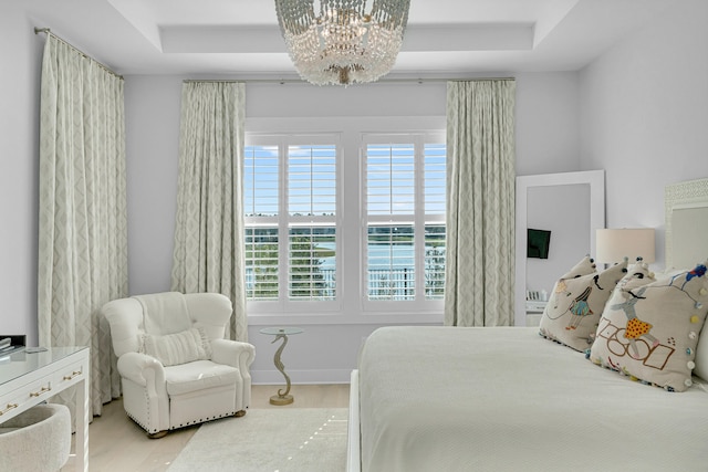 bedroom with a raised ceiling, hardwood / wood-style floors, and a chandelier