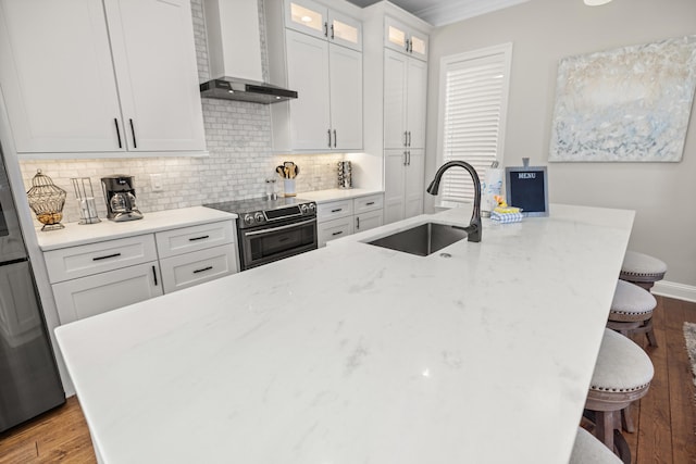 kitchen featuring sink, wall chimney exhaust hood, stainless steel appliances, a kitchen breakfast bar, and white cabinets