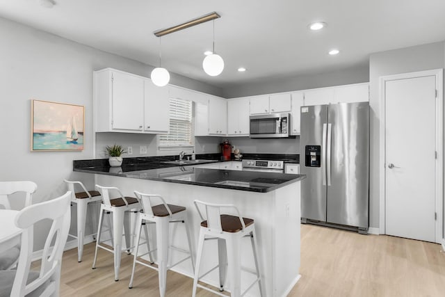 kitchen featuring kitchen peninsula, appliances with stainless steel finishes, light hardwood / wood-style flooring, white cabinetry, and a breakfast bar area