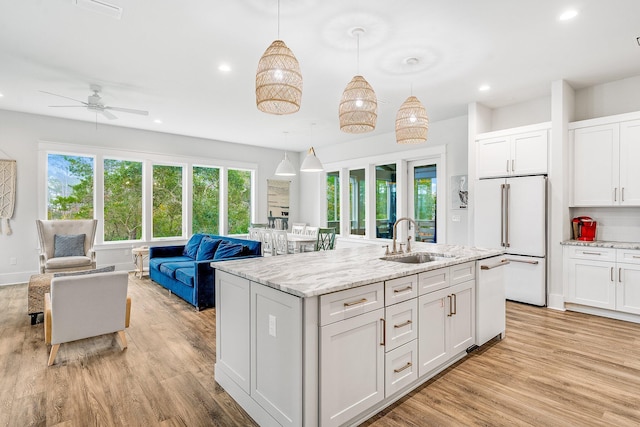 kitchen with white appliances, a kitchen island with sink, sink, decorative light fixtures, and white cabinetry