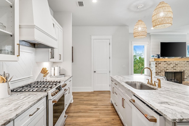 kitchen featuring high end white range, sink, stainless steel dishwasher, light wood-type flooring, and decorative light fixtures