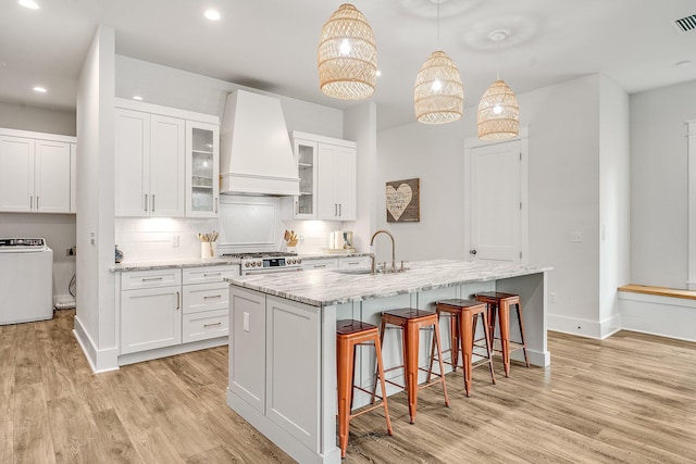 kitchen featuring washer / dryer, an island with sink, premium range hood, and sink