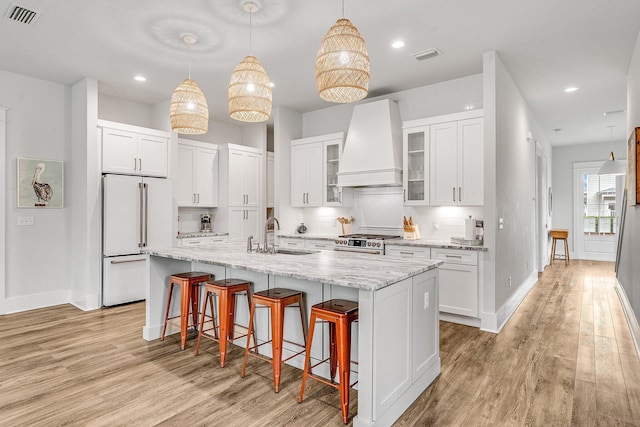 kitchen with premium range hood, gas stove, high end white refrigerator, sink, and a center island with sink