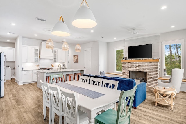 dining area with ceiling fan, sink, a fireplace, washer / dryer, and light hardwood / wood-style floors