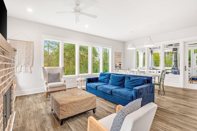 living room with light wood-type flooring, a brick fireplace, plenty of natural light, and ceiling fan