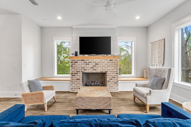 living room with hardwood / wood-style floors, ceiling fan, and a brick fireplace