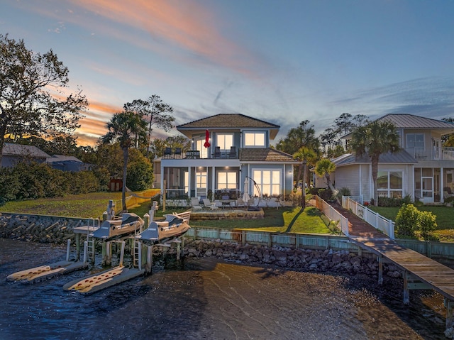 back house at dusk featuring a lawn and a balcony