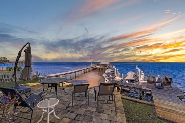 patio terrace at dusk featuring a dock and a water view