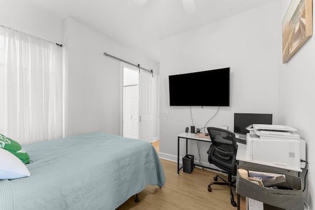 bedroom featuring a barn door, ceiling fan, and light wood-type flooring