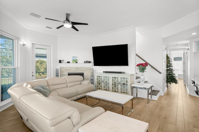 living room with a stone fireplace, crown molding, light hardwood / wood-style flooring, and ceiling fan