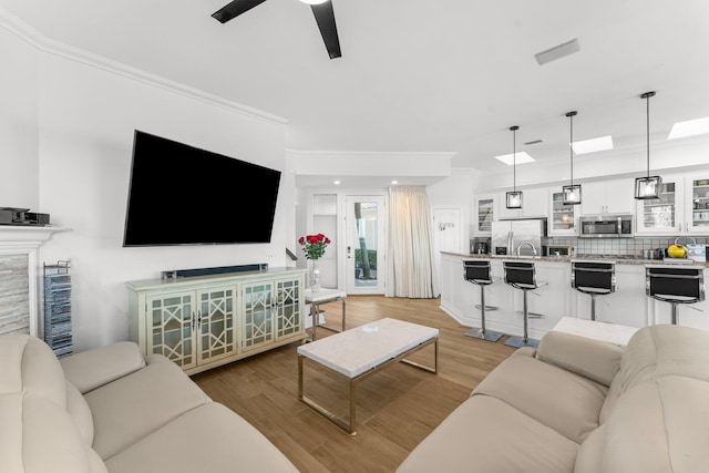 living room with ceiling fan, crown molding, and light wood-type flooring