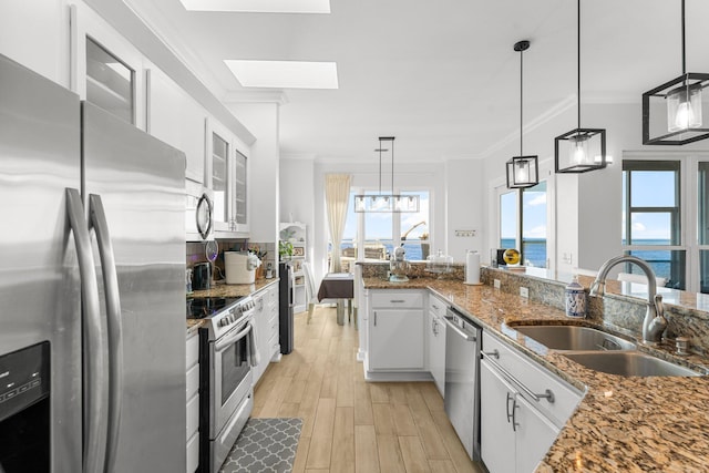 kitchen featuring a skylight, white cabinetry, sink, stainless steel appliances, and a water view