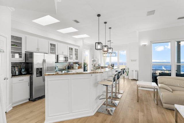 kitchen with a water view, white cabinets, light hardwood / wood-style floors, and appliances with stainless steel finishes