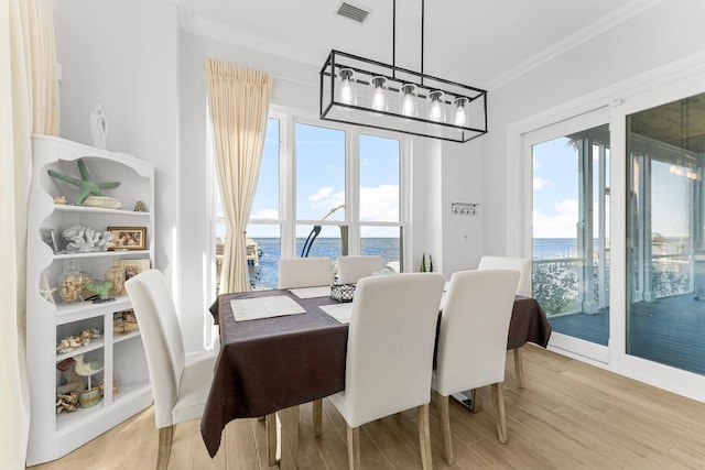 dining room with light hardwood / wood-style floors, a water view, a healthy amount of sunlight, and ornamental molding