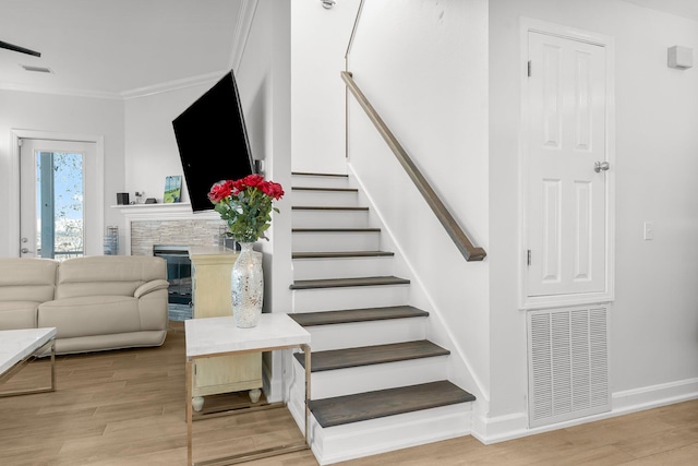 staircase with a stone fireplace, wood-type flooring, and ornamental molding