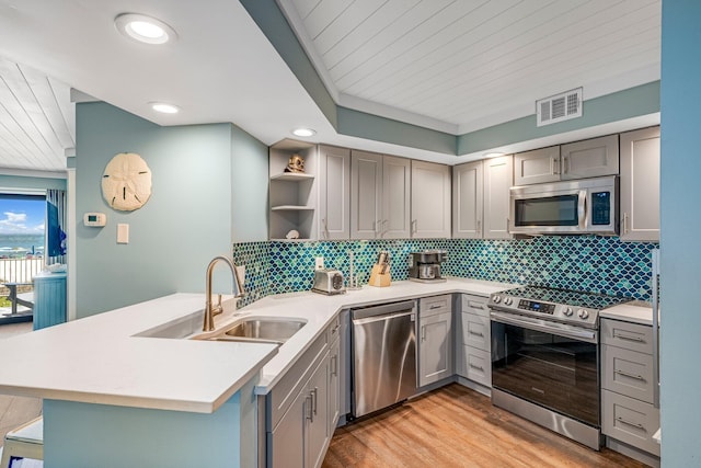 kitchen featuring sink, light wood-type flooring, a kitchen bar, kitchen peninsula, and stainless steel appliances