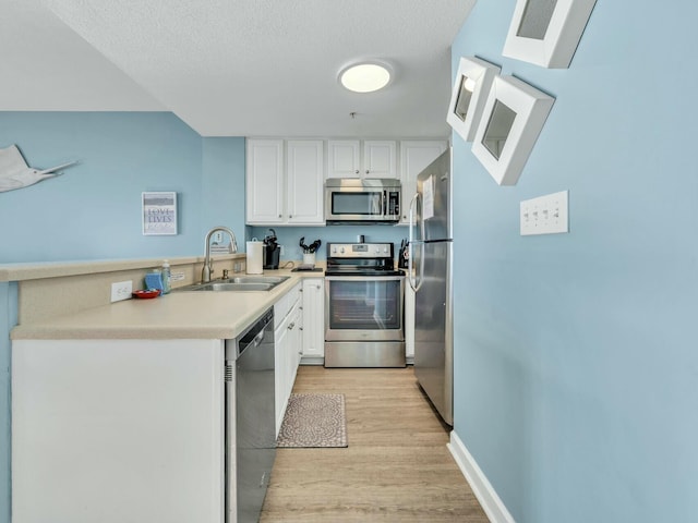 kitchen with a skylight, white cabinetry, sink, stainless steel appliances, and light hardwood / wood-style flooring