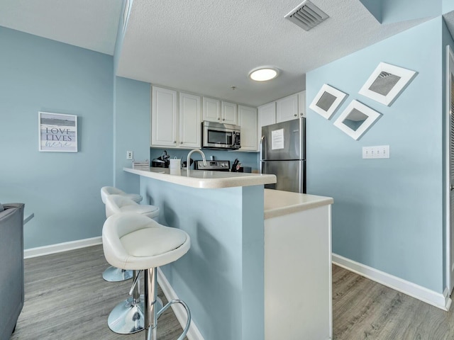 kitchen with a breakfast bar, white cabinets, light wood-type flooring, appliances with stainless steel finishes, and kitchen peninsula