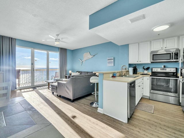 kitchen featuring appliances with stainless steel finishes, sink, a water view, white cabinets, and hardwood / wood-style floors