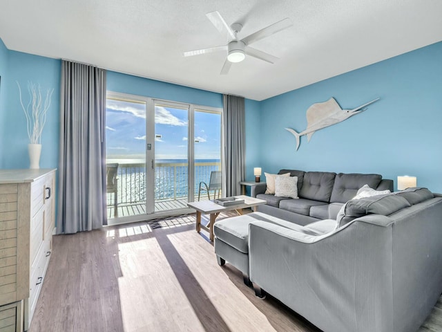 living room featuring ceiling fan, a water view, light hardwood / wood-style floors, and a textured ceiling