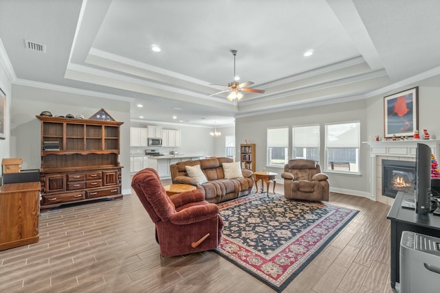 living room with a raised ceiling, ceiling fan, and ornamental molding