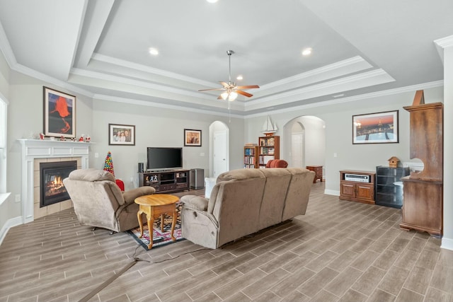 living room with a raised ceiling, ceiling fan, a fireplace, and ornamental molding