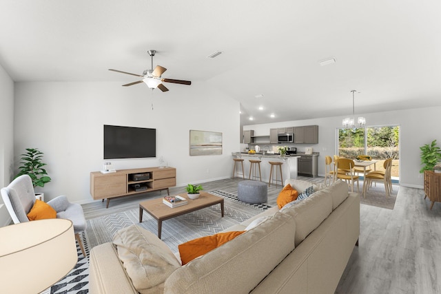 living room with ceiling fan with notable chandelier, light hardwood / wood-style floors, and vaulted ceiling