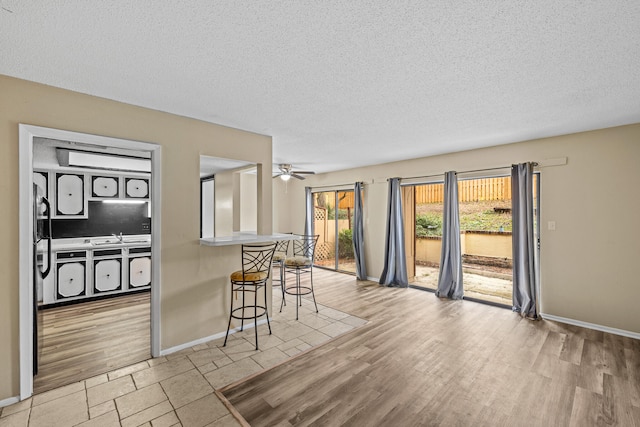 kitchen with ceiling fan, a kitchen bar, a textured ceiling, and light hardwood / wood-style flooring