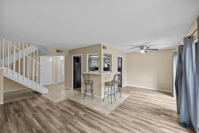 kitchen with a textured ceiling, ceiling fan, a breakfast bar area, and light hardwood / wood-style flooring