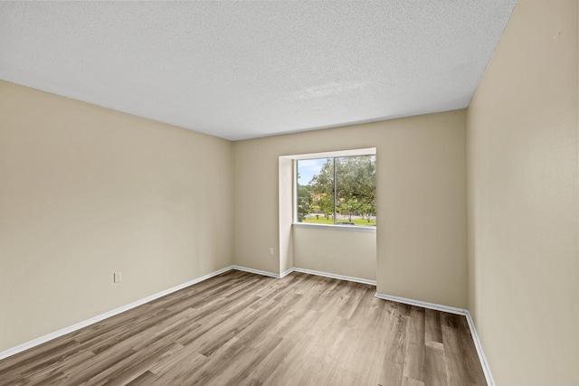 empty room with light wood-type flooring and a textured ceiling