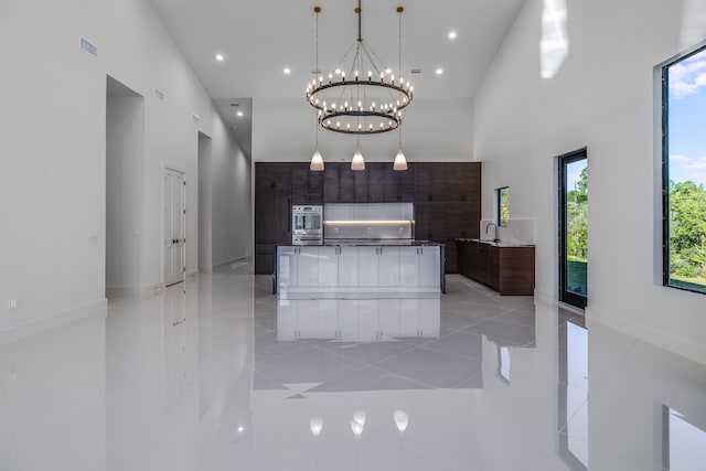 kitchen featuring a notable chandelier, a center island, dark brown cabinetry, and high vaulted ceiling