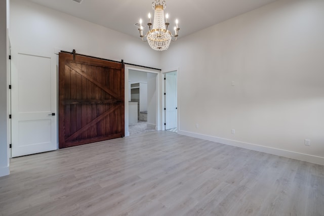 spare room with light wood-type flooring, a barn door, and a chandelier