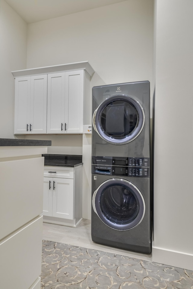 clothes washing area featuring stacked washer / drying machine, cabinets, and light wood-type flooring