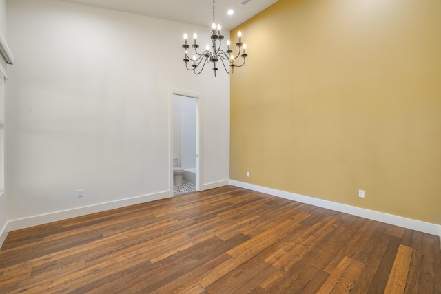 spare room featuring a towering ceiling, dark hardwood / wood-style floors, and an inviting chandelier