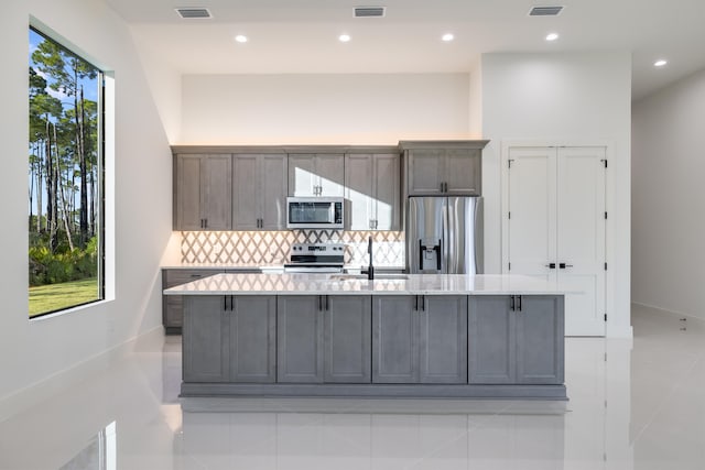 kitchen with appliances with stainless steel finishes, tasteful backsplash, a large island, and light tile patterned flooring