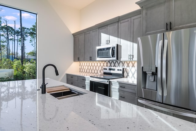 kitchen with sink, tasteful backsplash, light stone counters, gray cabinets, and appliances with stainless steel finishes