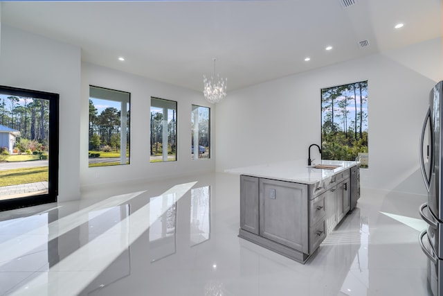 kitchen featuring a center island with sink, sink, hanging light fixtures, light stone countertops, and stainless steel refrigerator