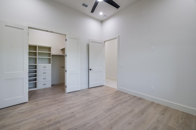 unfurnished bedroom with ceiling fan, a spacious closet, a high ceiling, and light wood-type flooring