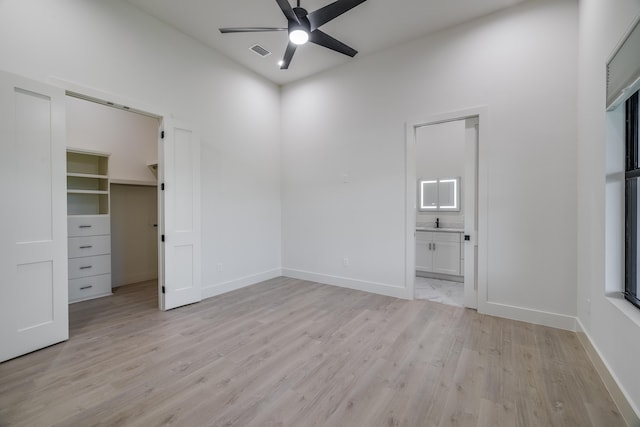 unfurnished bedroom with ceiling fan, light hardwood / wood-style floors, a spacious closet, and ensuite bath