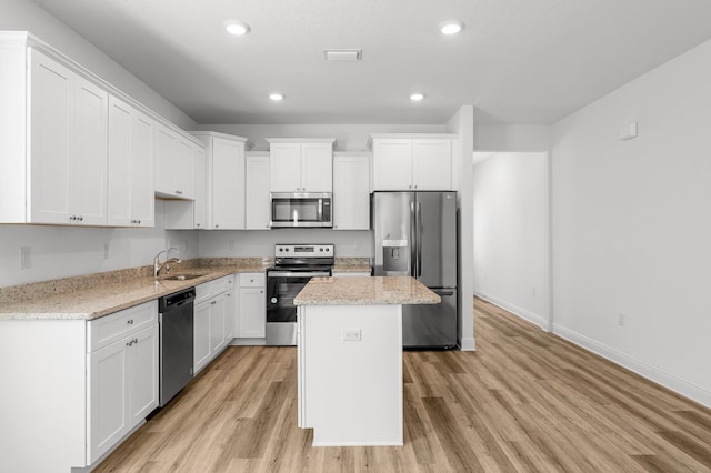 kitchen with appliances with stainless steel finishes, light wood-type flooring, sink, white cabinets, and a center island