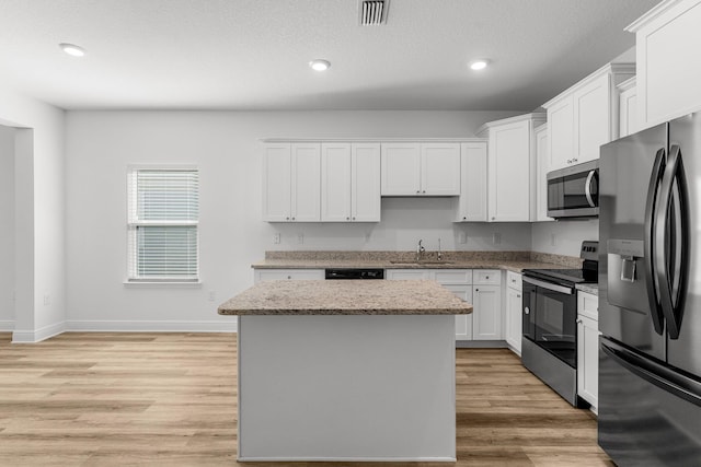 kitchen with a center island, light stone countertops, light wood-type flooring, white cabinetry, and stainless steel appliances