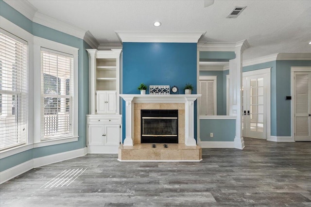 unfurnished living room with wood-type flooring, a textured ceiling, a tile fireplace, and ornamental molding